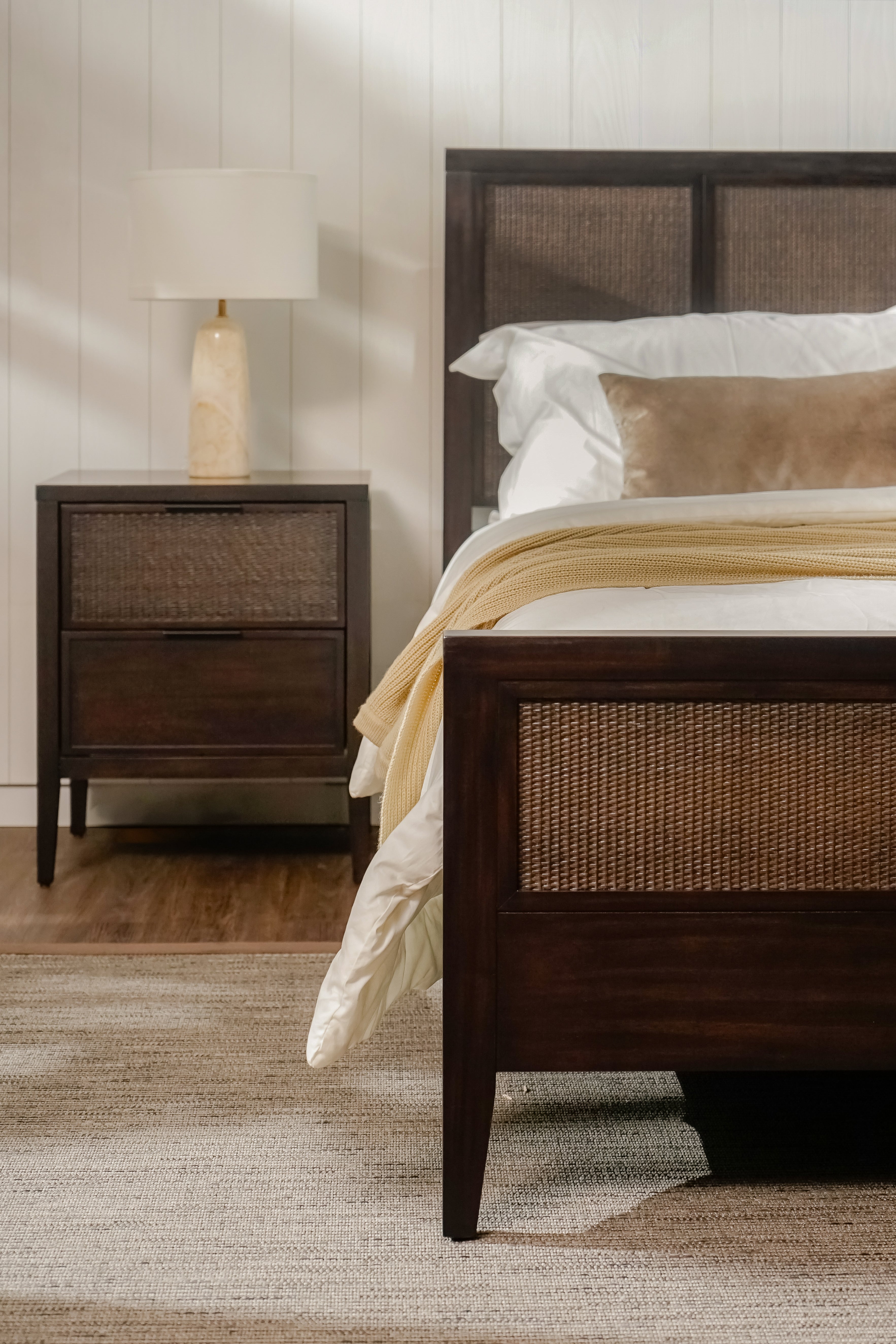 Bedroom with wooden bed and Black Kalana - 2-Drawer Rattan Nightstand against a neutral wall.