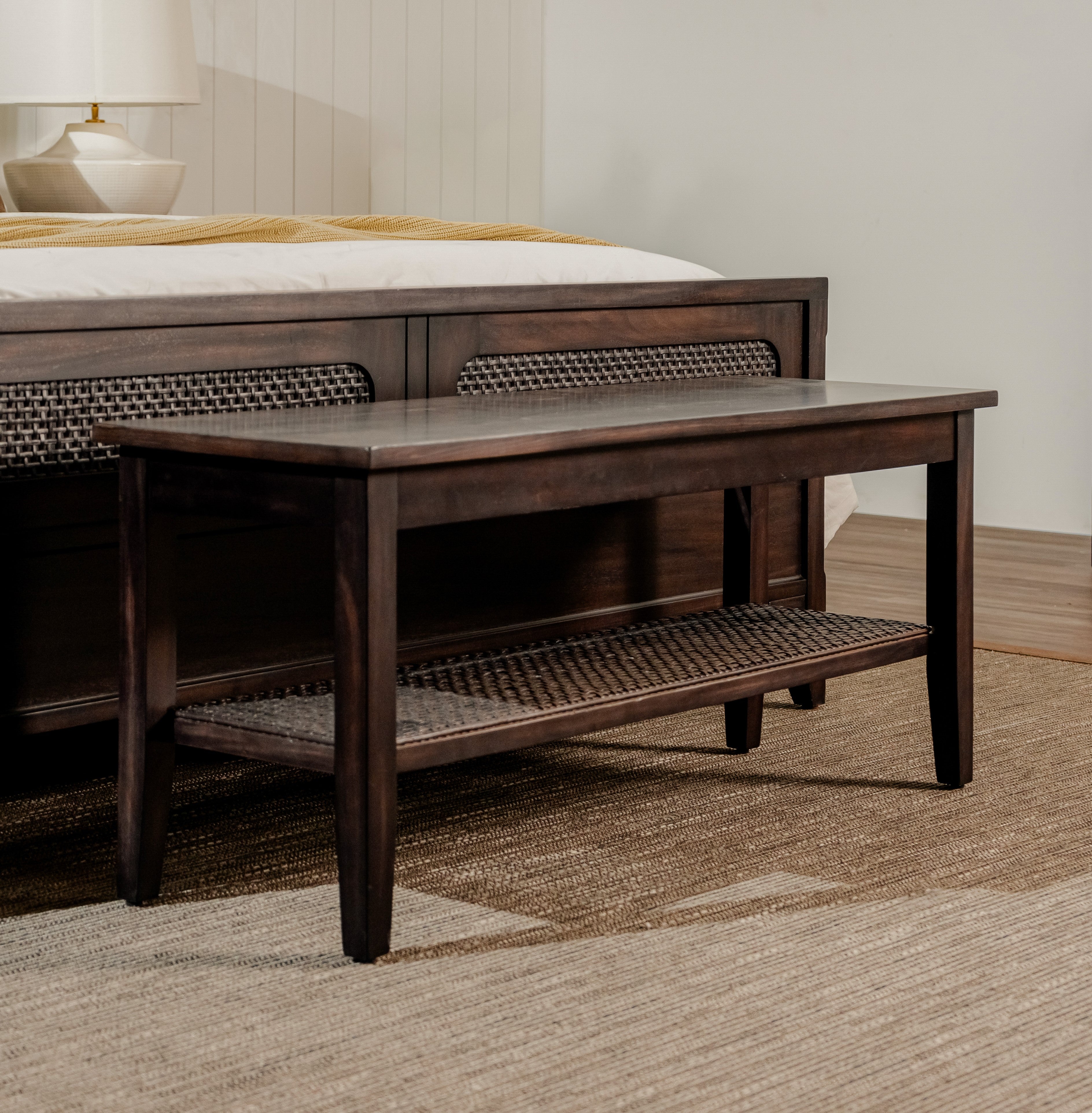 Wooden bench in front of a bed with wicker backrests in a bedroom setting.