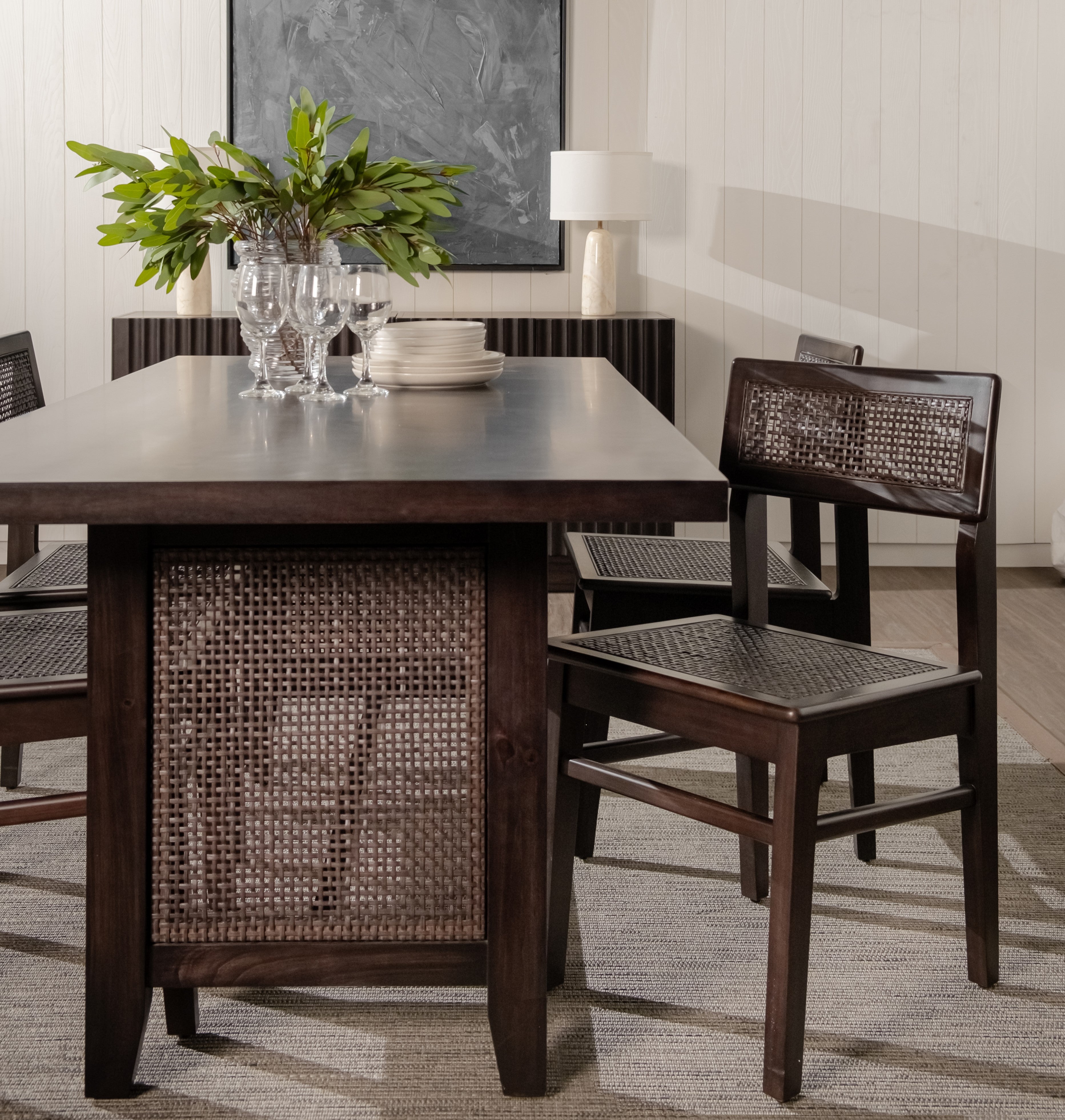 Dining room with a dark wooden table and chairs, featuring a plant and wine glasses.