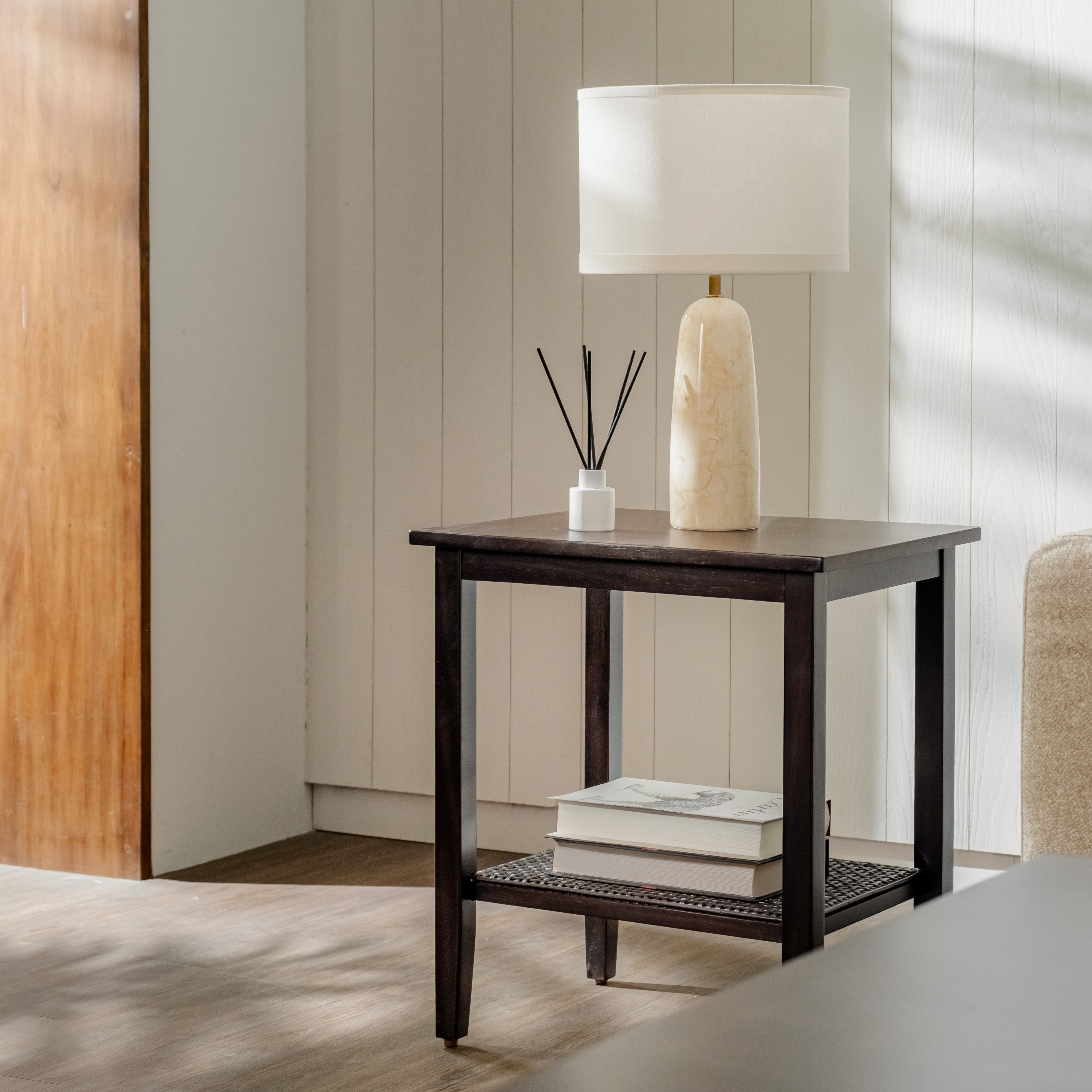Dark wooden side table with a lamp, books, and diffuser in a room with wooden flooring and wall.