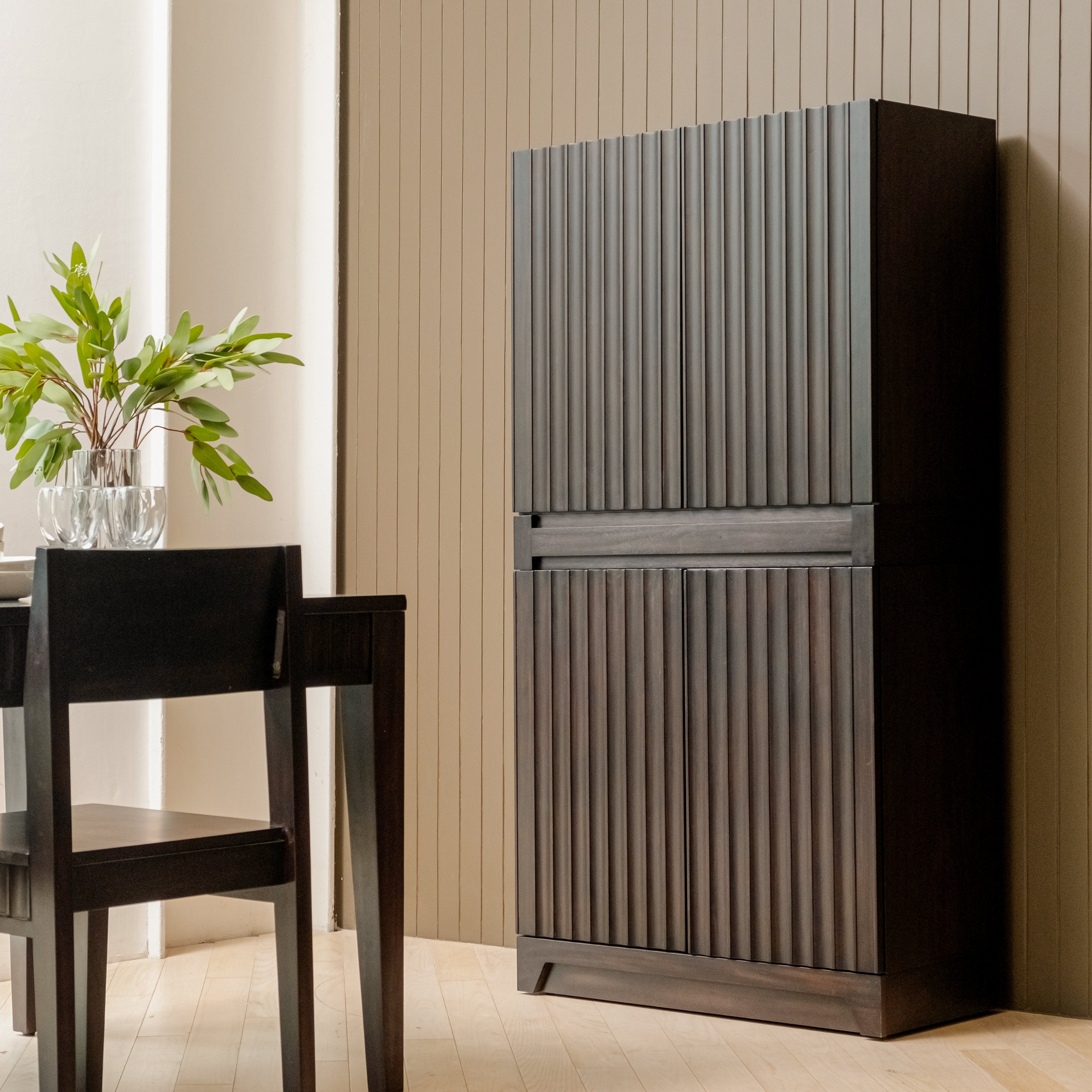 Wooden cabinet with ribbed design next to a dining table with chairs in a room.