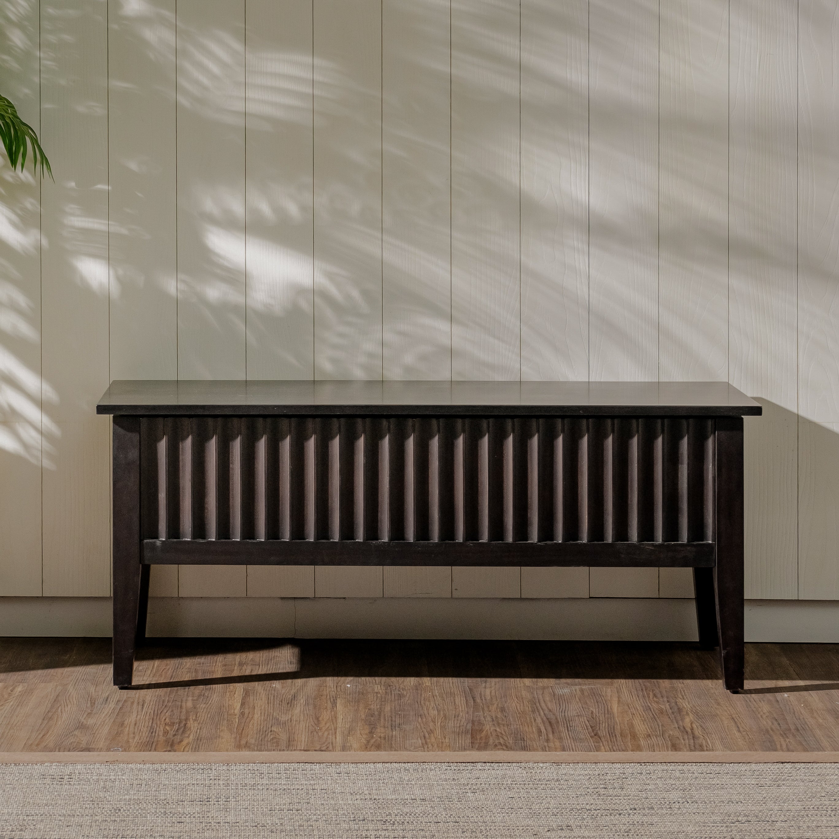 Dark wooden bench against a light paneled wall with natural light casting shadows.