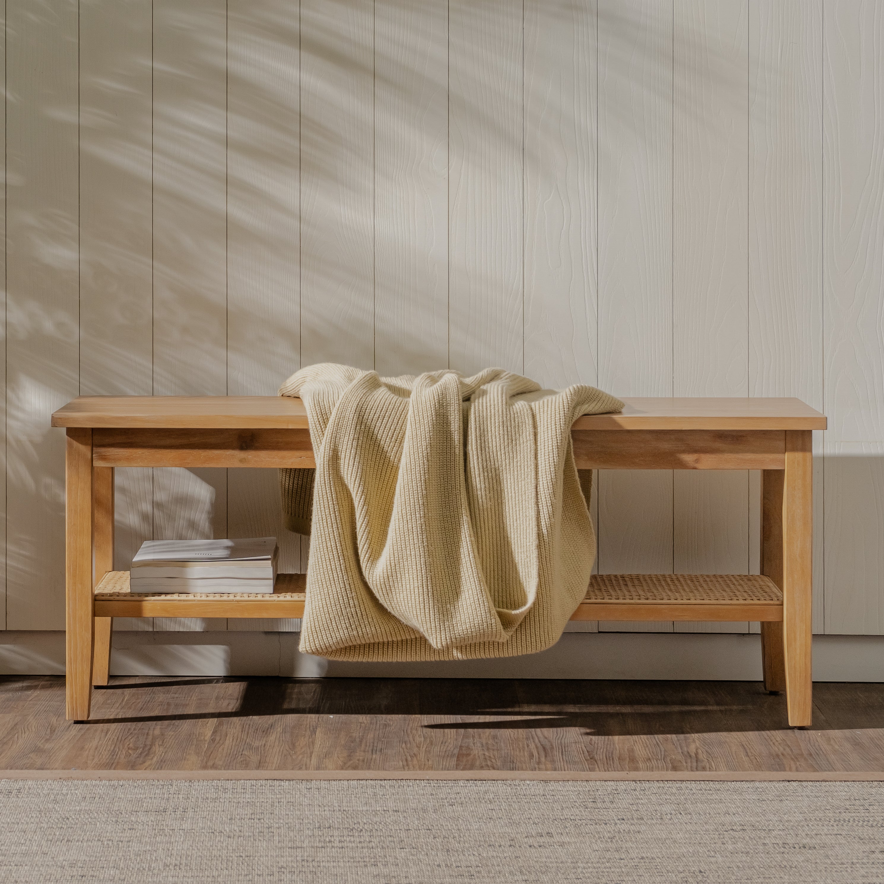 Wooden bench with a beige blanket draped over it against a neutral wall.