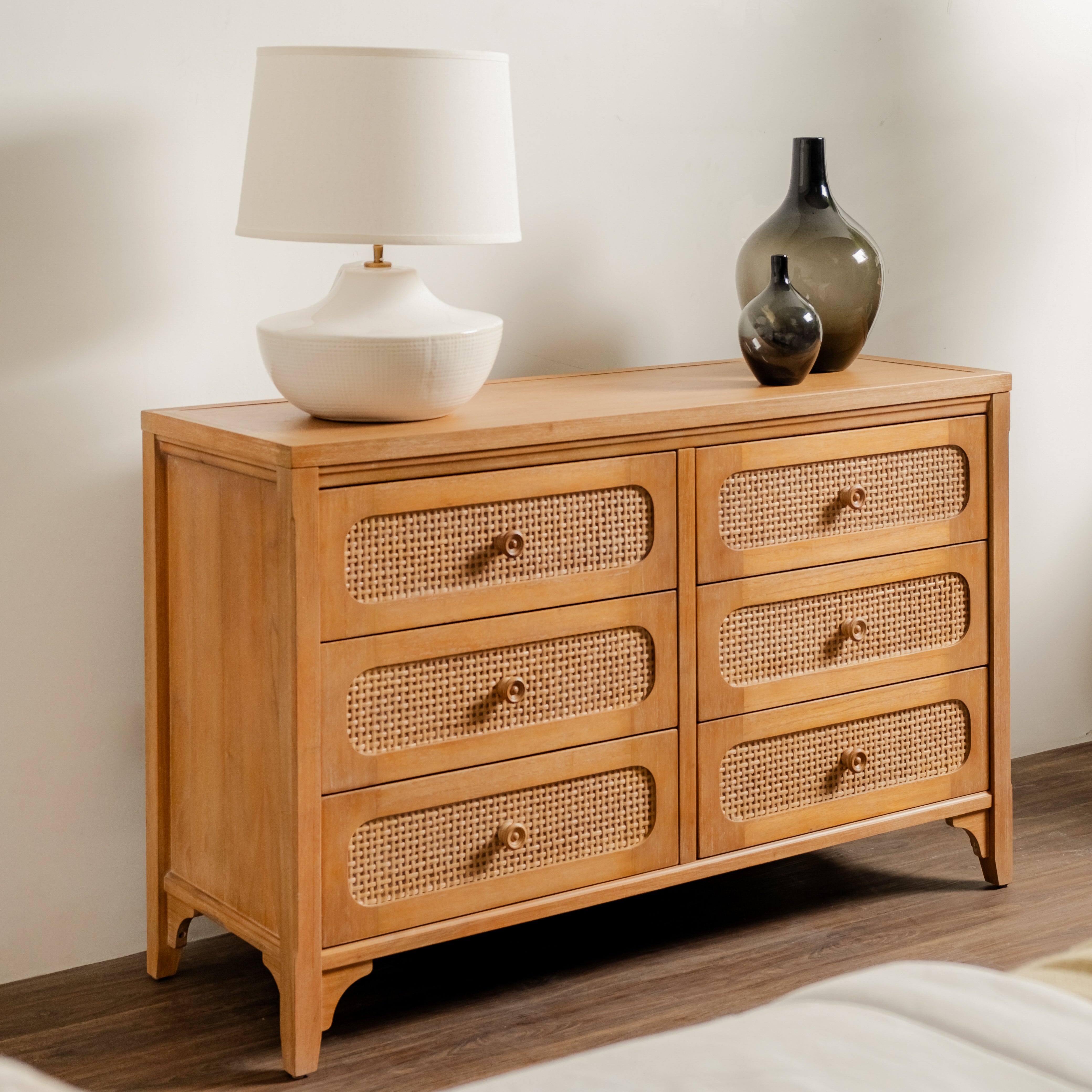 Wooden dresser with wicker drawers, lamp, and decorative vases on a neutral background