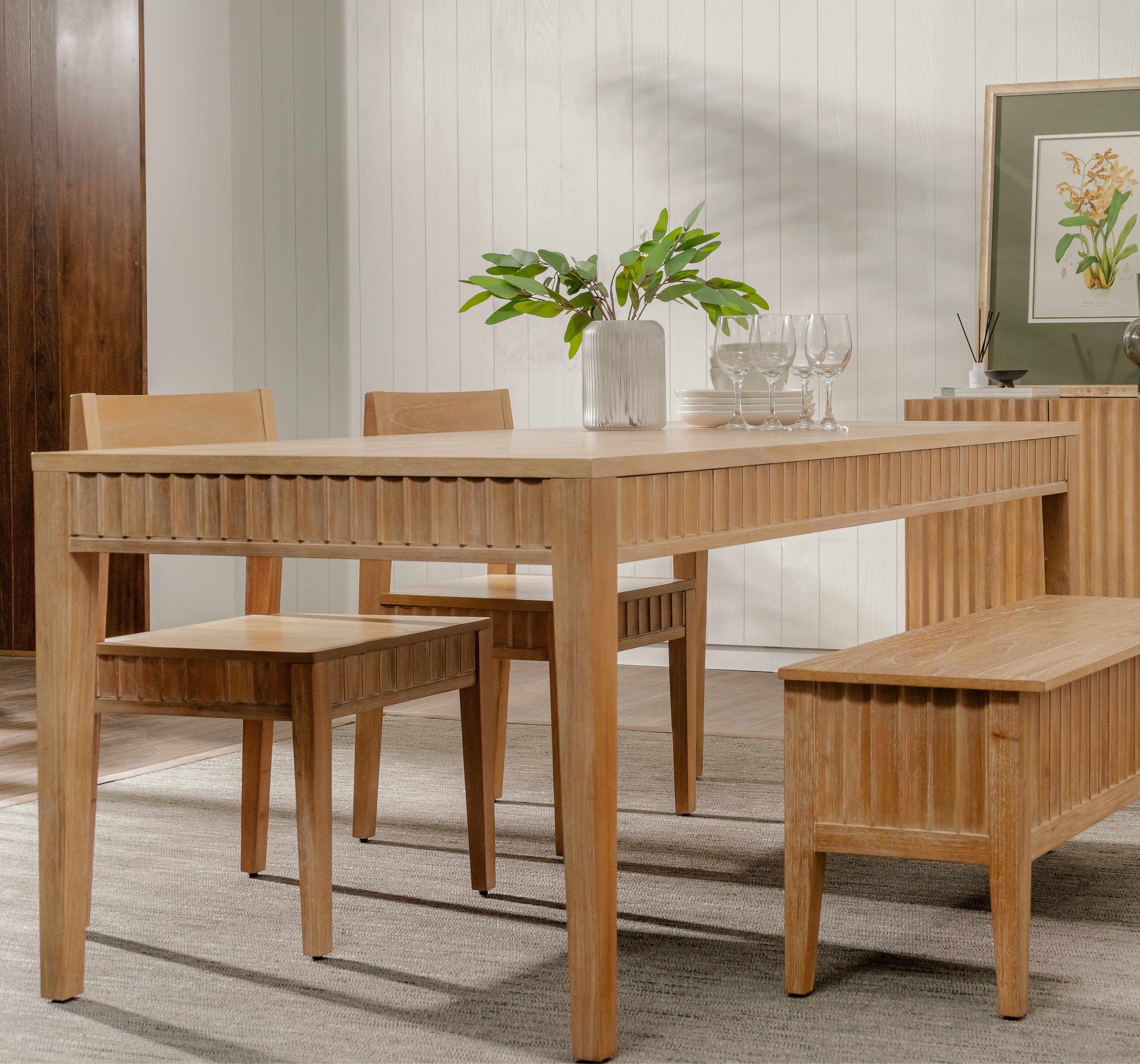 Wooden dining set with table, chairs, and bench in a room with a plant and framed picture.