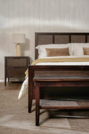 Bedroom with wooden bed, nightstand, and lamp against a light wall.
