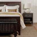 Wooden bed with white bedding and a nightstand with a lamp in a bedroom setting.