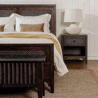 Wooden bed with white bedding and a nightstand with a lamp in a bedroom setting.