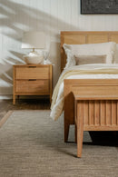 Wooden bed and nightstand in a bedroom setting with neutral decor.