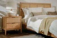 Wooden bed with white bedding and a nightstand with a lamp in a bedroom setting.